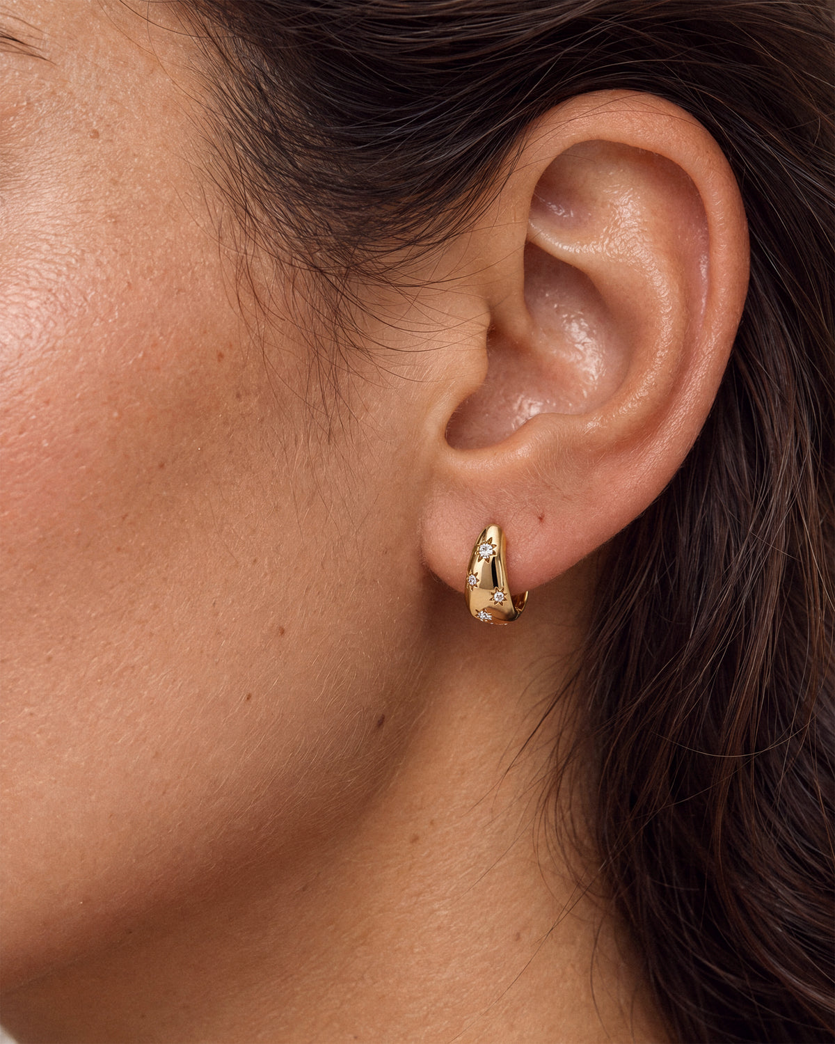 A model wearing an 18k gold vermeil huggie hoop earring with star-shaped clear white diamond CZs.