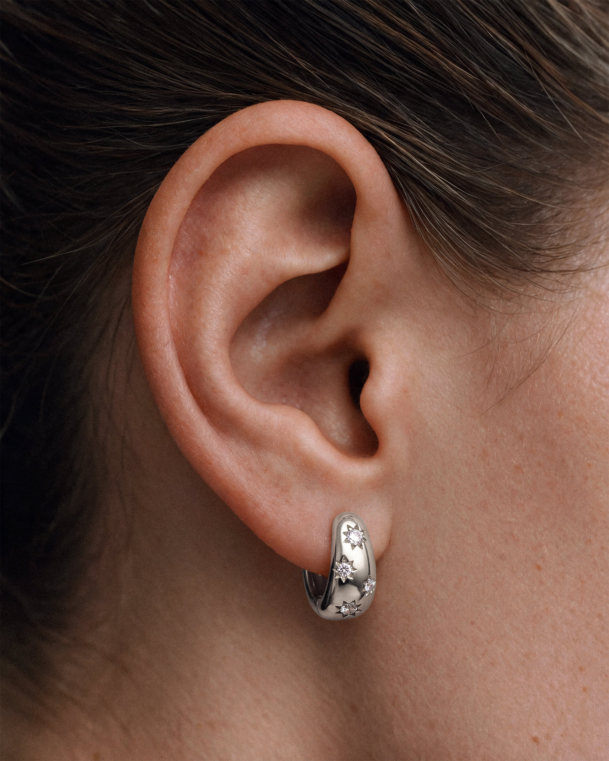 A model wearing a 925 sterling silver chunky huggie hoop earring with star-shaped cz diamond accents.