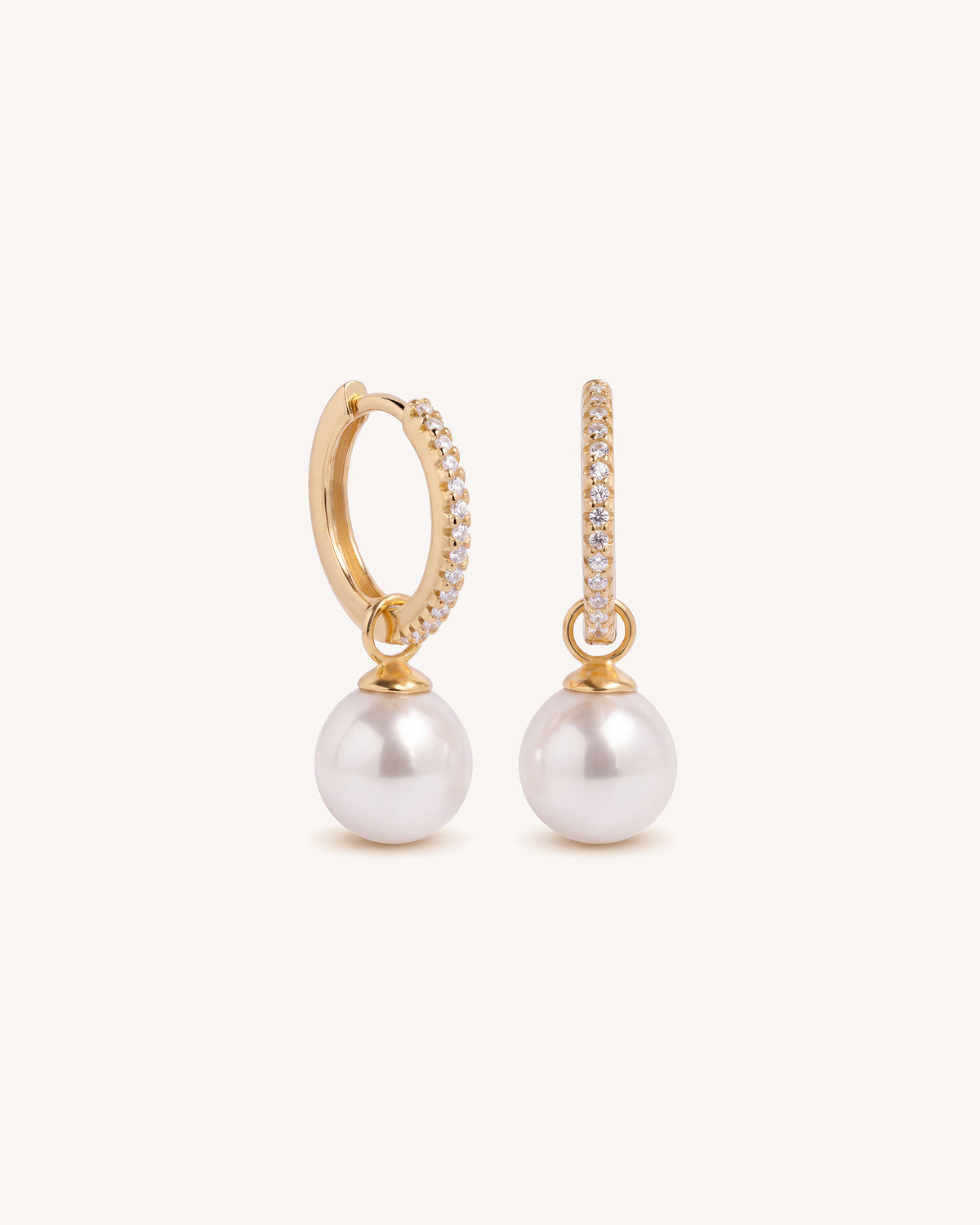 A pair of gold hoop earrings with small clear pavé accents and dangling white pearls, shown on a clean off-white background.