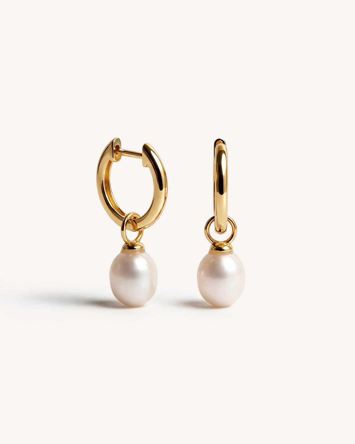 A pair of 18k gold hoop earrings with dangling white freshwater pearls, shown on a clean off-white background.