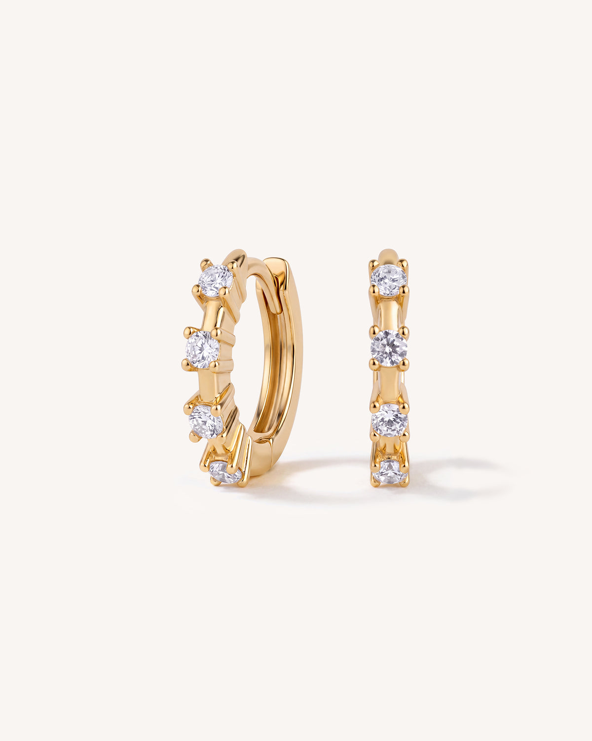A pair of gold huggie hoop earrings with a row of clear round-cut stones, shown on a clean off-white background.