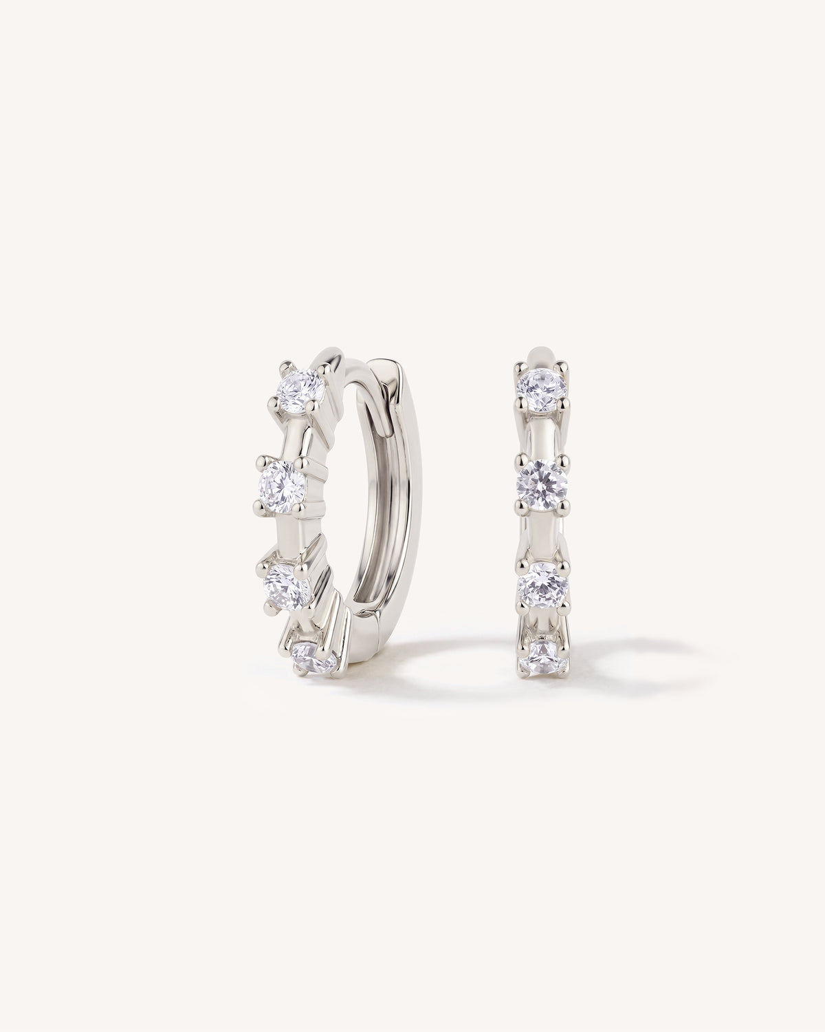 A pair of silver huggie hoop earrings with clear cubic zirconia stones, displayed on a clean off-white background.