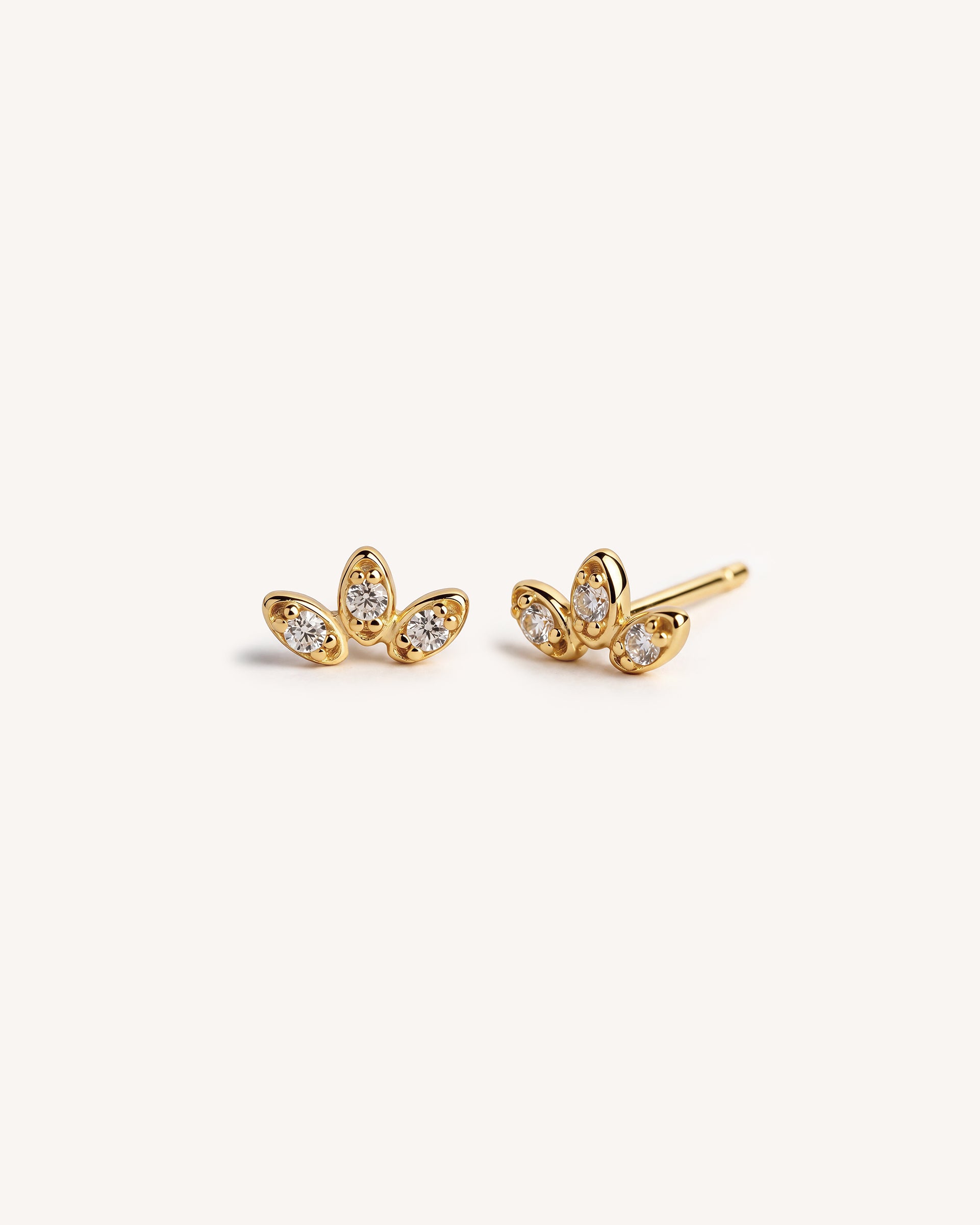 A pair of 18k gold plated 925 sterling silver stud earrings with marquise-cut clear gemstones arranged in a small leaf or cluster or petal shape, photographed on a clean off-white background.