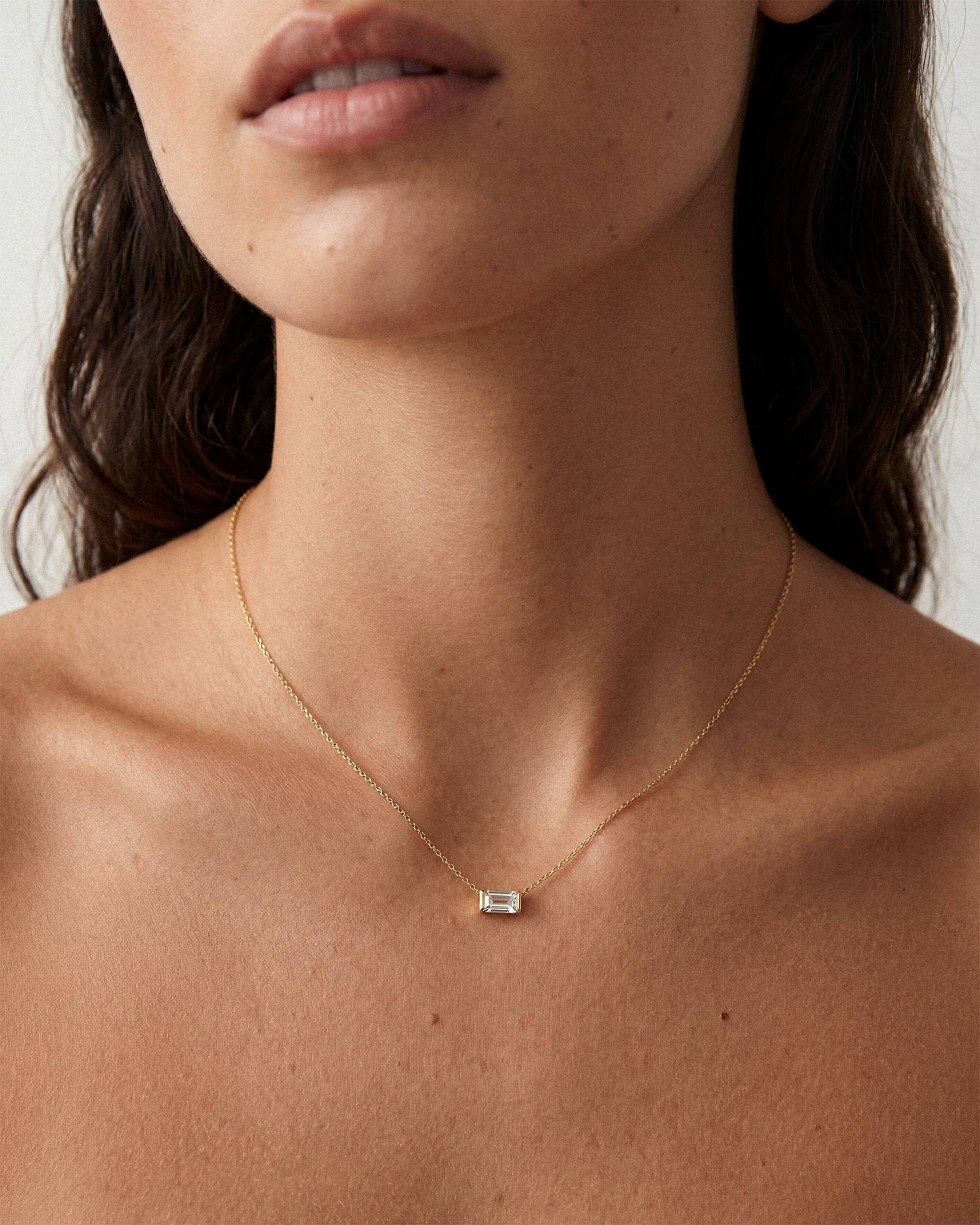 Gold necklace with a small pendant on a person's neck against a neutral background