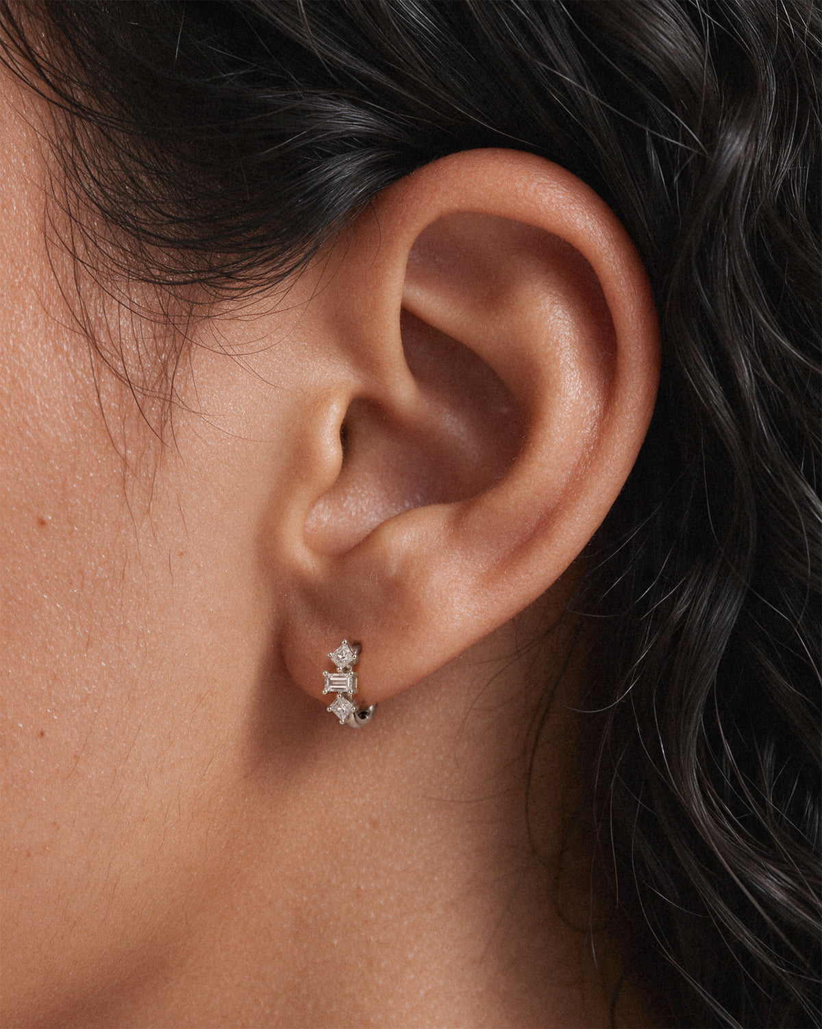 Baguette Trinity Huggie Hoops in 925 Sterling Silver worn on the earlobe — close-up of baguette and princess-cut crystal huggie earrings