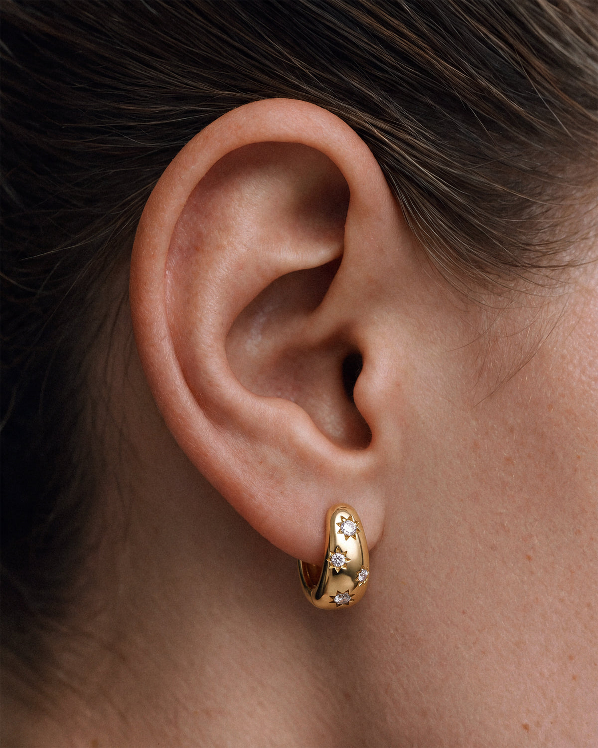 A model wearing an 18k gold vermeil huggie hoop earring with star-shaped diamond CZs.