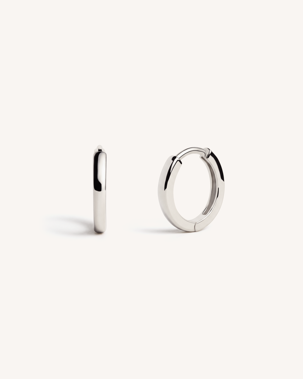 A pair of polished 925 sterling silver huggie hoop earrings shown on a clean, off-white background, with one earring standing vertically to show its side profile and the other lying horizontally to show its front and back. A bestseller. 