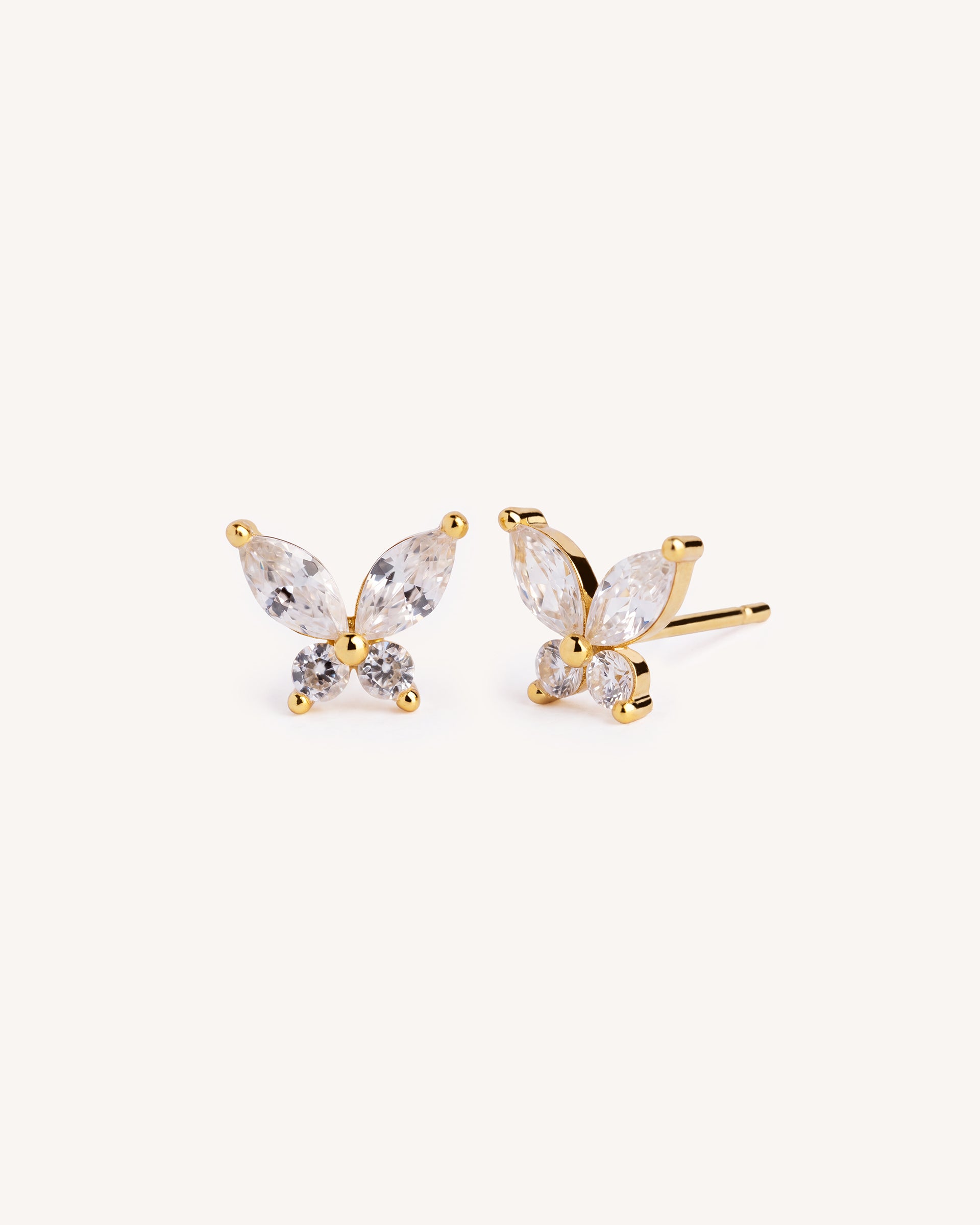 A pair of gold butterfly stud earrings with marquise-cut clear crystals, shown on a plain off-white background.