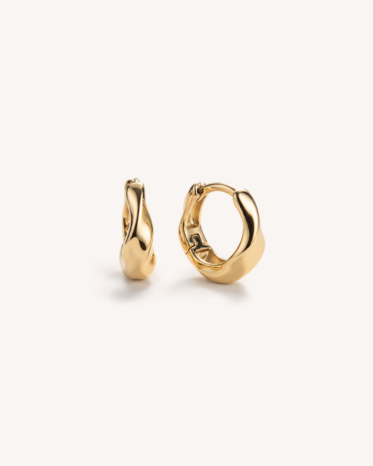 A pair of polished gold molten huggie hoop earrings with a unique organic, wavy shape, displayed on a clean off-white background.