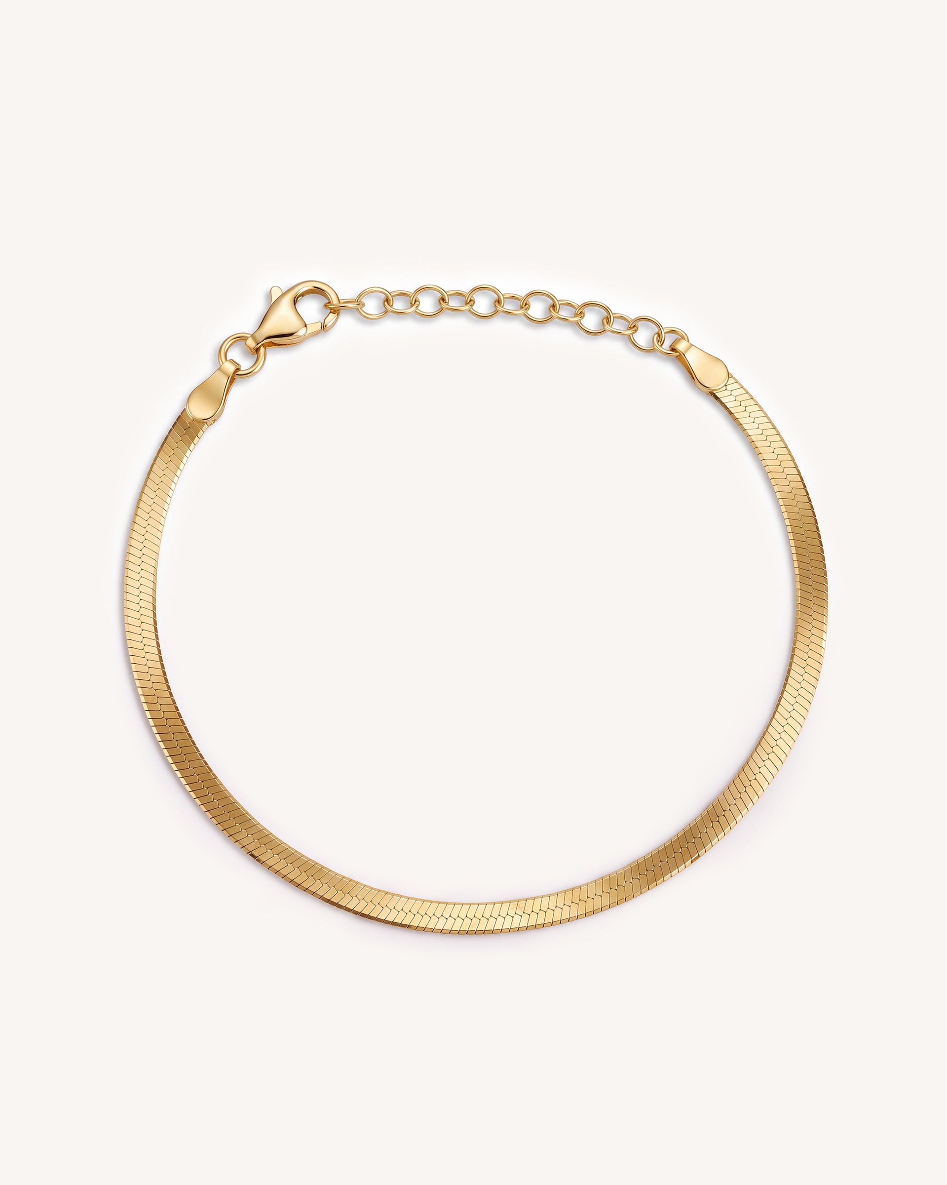 A gold-toned snake chain bracelet with a herringbone pattern and a lobster clasp and extension chain, displayed on a clean off-white background.
