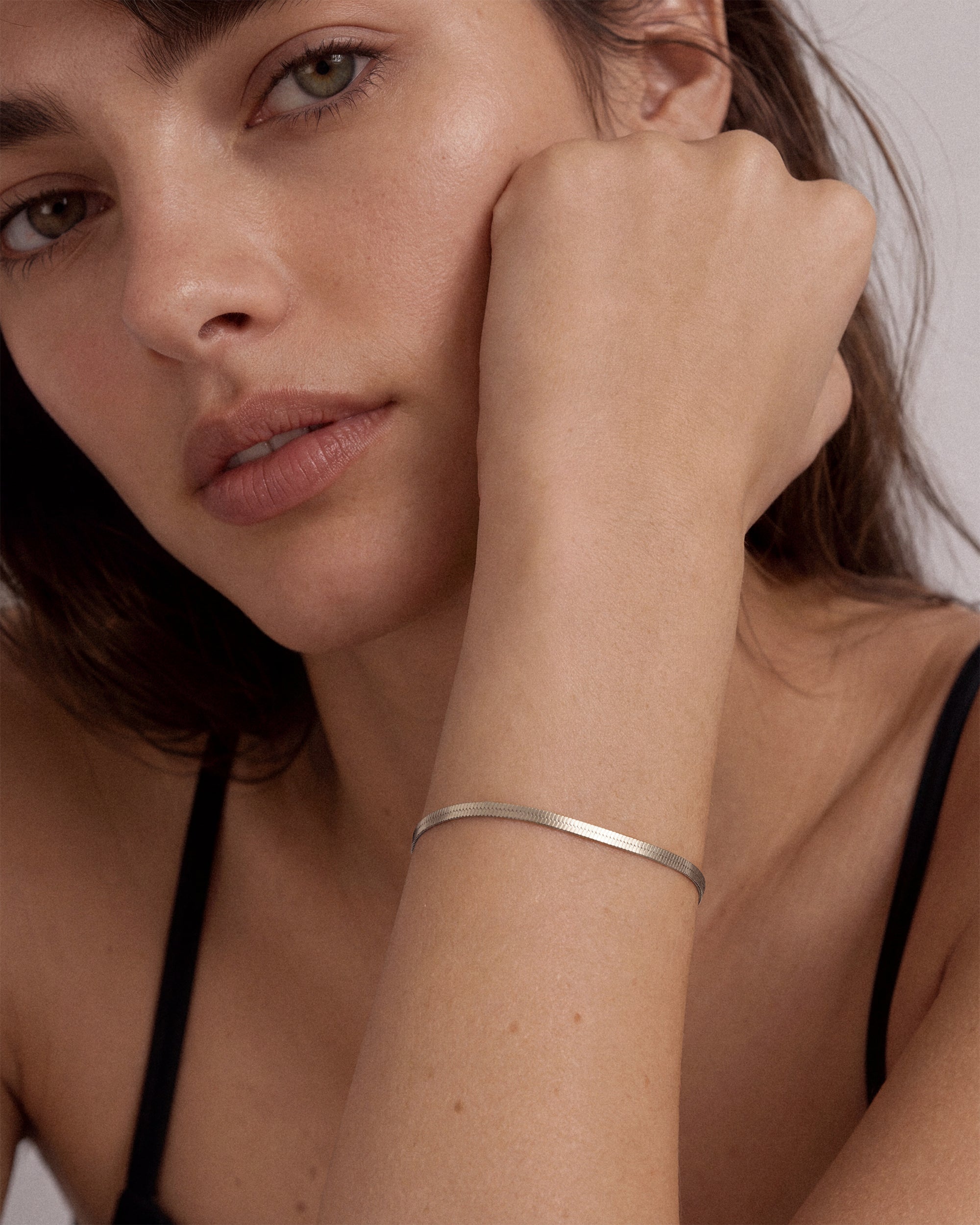A close-up of a woman's wrist wearing a thin, polished 925 sterling silver snake chain bracelet.