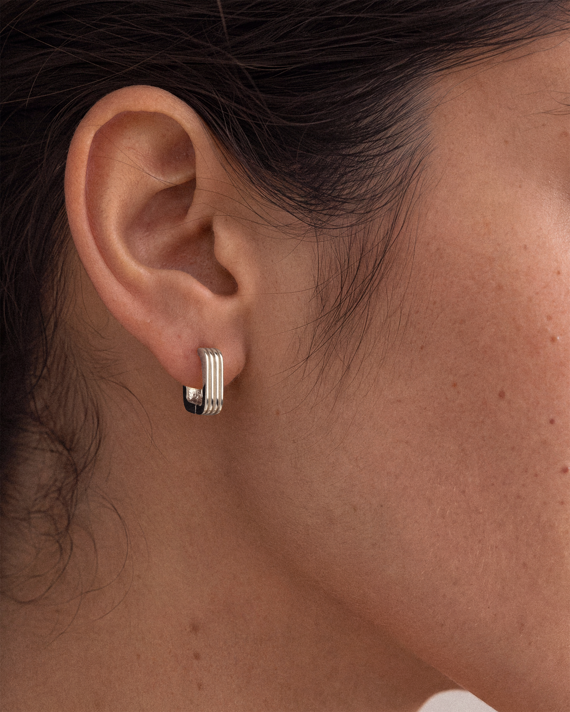 A close-up of a person's ear wearing a small 925 silver huggie hoop earring with three parallel vertical ridges on the front.