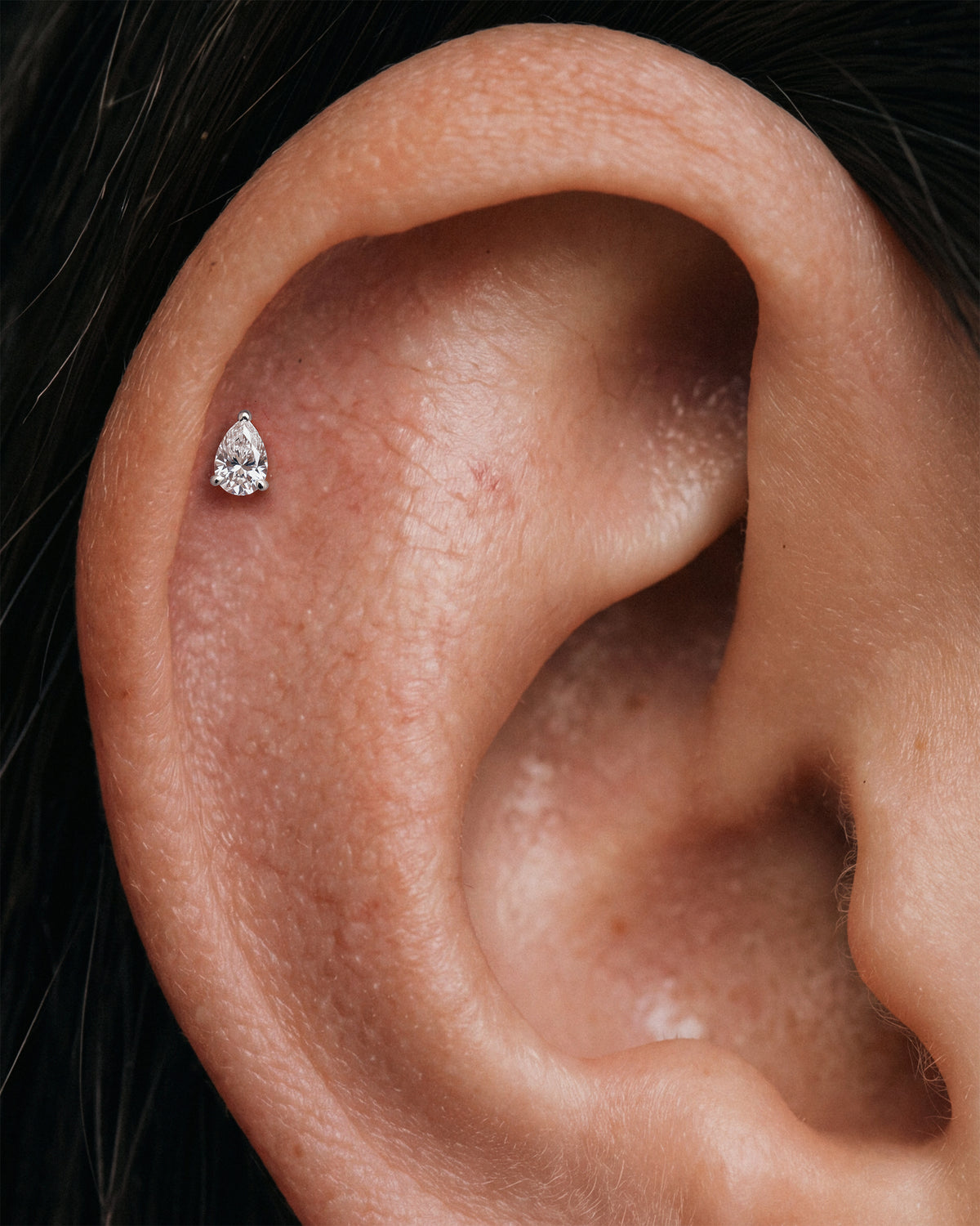 Close-up of a model's ear wearing two tiny 925 sterling silver ear stud, flatback earrings with clear gemstones on her upper helix piercings.
