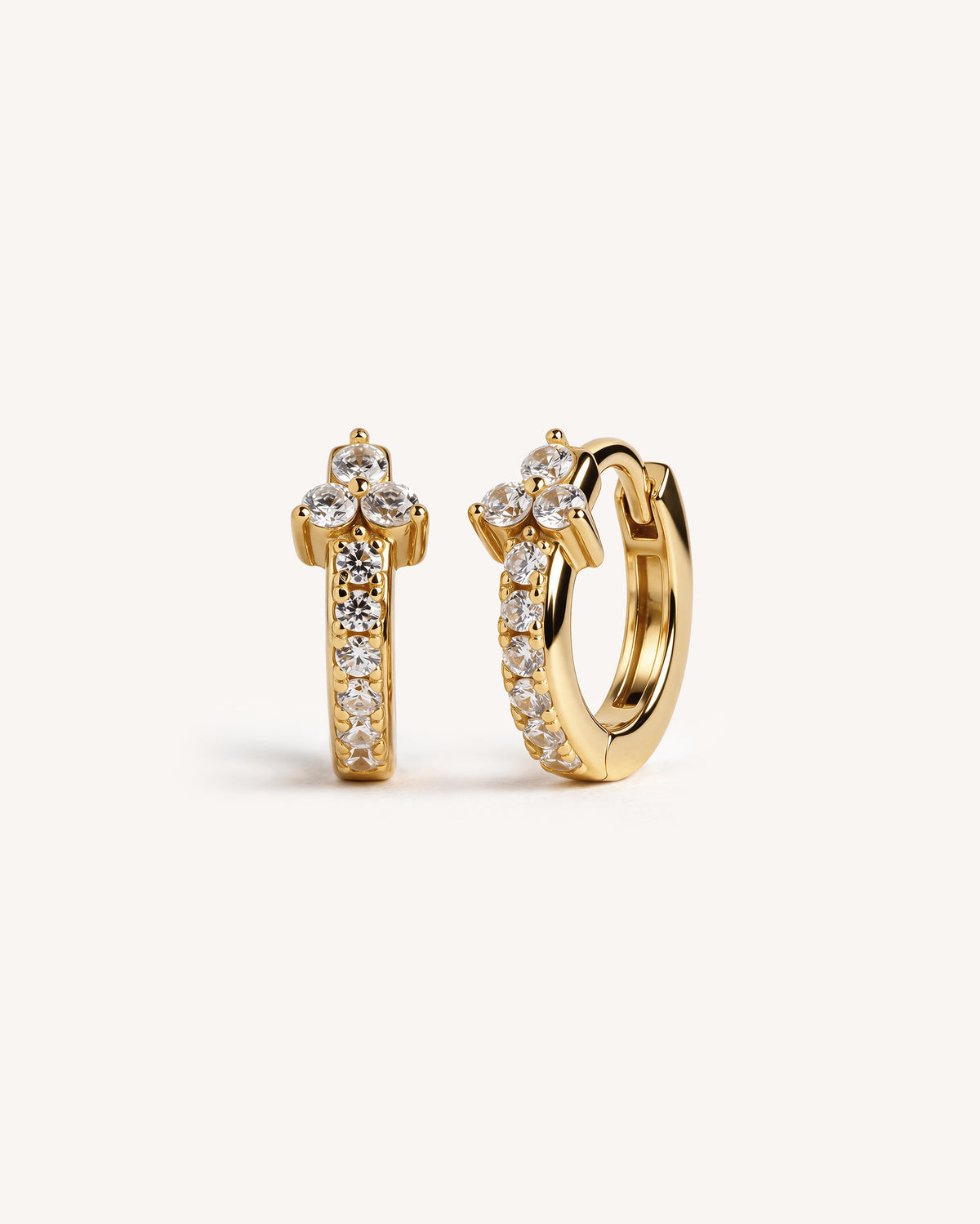 A pair of gold huggie hoop earrings with a floral crown design and pavé-set clear stones, shown on a clean off-white background.